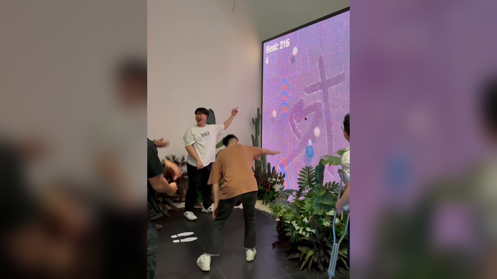 Two players in front of the LED wall mid-game: one laughs and points while the other swings his arm towards fruit on the screen, which shows a best score of 216